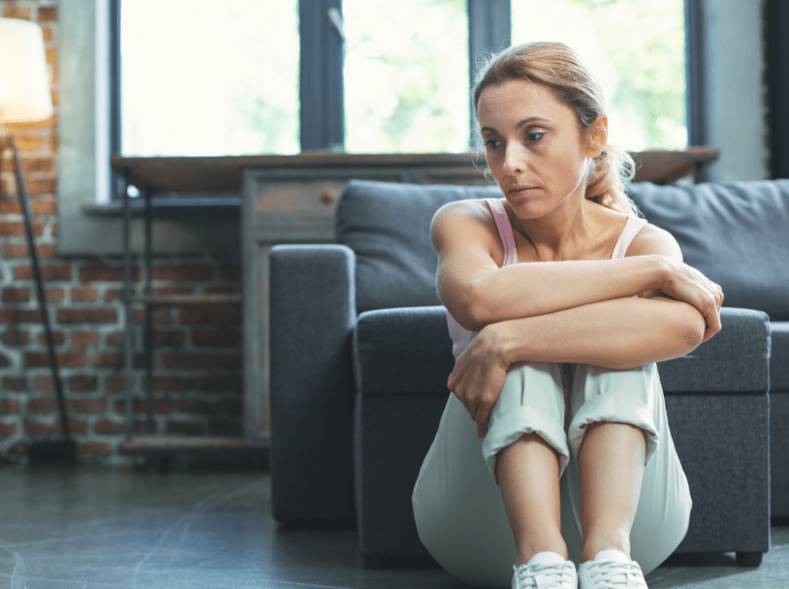 Mulher em idade de menopausa é vista pensativa na sala de sua casa: conheça os desafios e mudanças na menopausa
