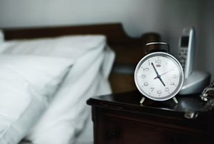 Relógio próximo a uma cama; o tratamento da noctúria depende da causa: quando está relacionada à próstata aumentada, existem várias opções.